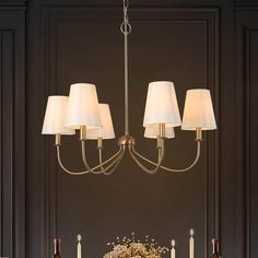 a chandelier hanging over a dining room table with candles and flowers on it