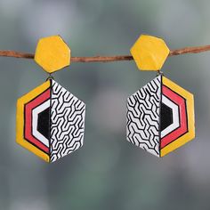 pair of earrings with geometric designs hanging from a line on a branch in front of blurry background