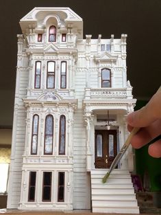 a hand is holding a paintbrush in front of a model house that looks like it has been built