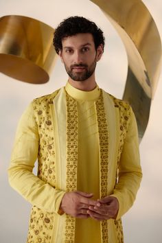 Summer Love Shrug Set | Jatin Malik Introducing our vibrant lemon yellow shrug set, adorned with intricate floral hand embroidery and three types of embroidered lapels in shades of yellow. This ensemble radiates freshness and sophistication, capturing attention with its intricate detailing and vibrant color palette. Paired with an embroidered shoulder-button kurta and tapered trousers, this outfit offers a perfect balance of elegance and contemporary style. Ideal for special occasions, this ensemble is sure to make a statement with its unique design and impeccable craftsmanship. Included in purchase: Shrug Set, Kurta, Trousers Product Specification Color: Yellow Fabric: Linen Silk Occasion: Engagement, Wedding, Bridal, Reception Style: Shrug Set, Kurta, Trousers Care: Dry Clean Work: Hand Designer Yellow Sets With Chikankari Embroidery, Yellow Sets With Chikankari Embroidery, Transitional Designer Wear Yellow Sherwani, Traditional Yellow Sherwani For Designer Wear, Yellow Bandhgala With Zari Work For Designer Wear, Designer Sets With Floral Embroidery And Traditional Drape, Designer Yellow Sherwani For Eid, Yellow Embroidered Kurta For Reception, Designer Yellow Sherwani For Diwali