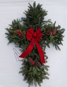 a cross made out of pine cones and red ribbon on a white background with the word christmas written below it