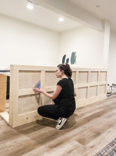 a woman sitting on the floor next to a large wooden shelf with books in it