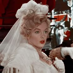 a woman in a white wedding dress and veil with red lipstick on her lips is looking at the camera