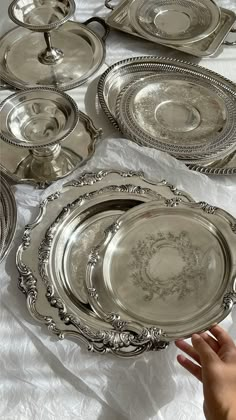 a table topped with lots of shiny silver plates and bowls on top of a white cloth