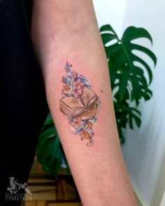 a person with a tattoo on their arm holding an open book and flowers around it