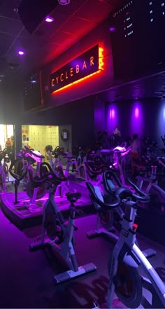 there are many exercise bikes in the gym with neon lights around them and people walking by