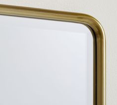 a gold framed mirror hanging on the wall with a white wall in the back ground