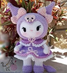 a crocheted stuffed animal wearing a purple and white dress sitting next to a potted plant