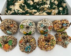 six donuts with different toppings are in a white box next to a green cake