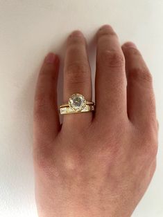 a person's hand wearing a gold ring with a white diamond in the middle