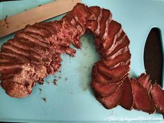 a piece of meat sitting on top of a blue cutting board next to a knife