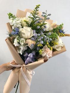 a bouquet of flowers wrapped in brown paper with a ribbon tied around the end, held by someone's hand