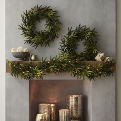 two wreaths are hanging on the mantle above candles