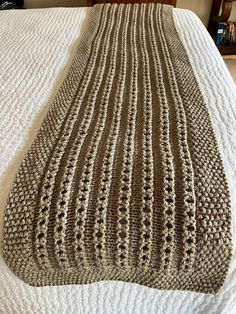 a crocheted blanket on top of a bed with white sheets and brown headboard