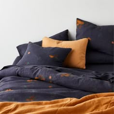 a bed with blue and orange sheets, pillows and blankets on top of it in front of a white wall