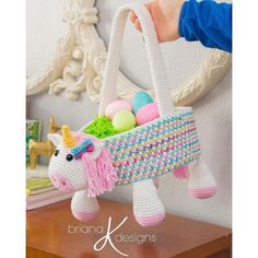 a crocheted unicorn carrying a basket filled with eggs on top of a table