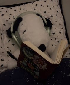 a stuffed panda bear with headphones reading a book on a bed covered in stars