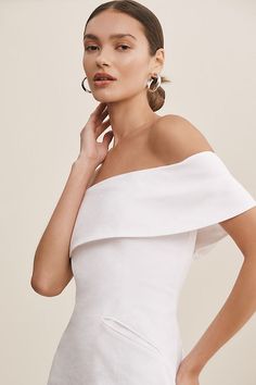 a woman in a white dress posing with her hands on her chin and wearing earrings