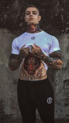 a man with tattoos standing in front of a wall