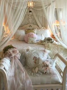 a white bed covered in lots of pillows and blankets next to a chandelier