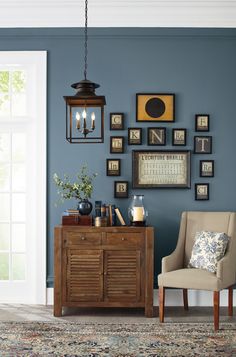 a living room with blue walls and pictures on the wall, a beige chair in front of a wooden cabinet