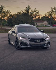 the front end of a silver acurace in a parking lot with trees in the background