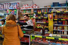 a man and woman standing in front of a store filled with food items, talking to each other