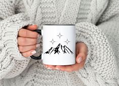 a woman is holding a coffee mug with mountains on the front and stars in the middle