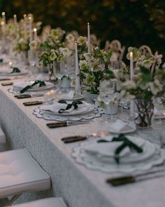 a long table set with white plates and flowers on it for an elegant dinner party