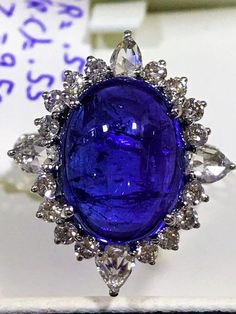 This tanzanite cabochon promise ring or anniversary ring is crafted in solid 18k white gold. The timeless and classic design of this beautiful ring will make your engagement or wedding unforgettable.SETTING :-Gross Weight: 4.054 gramsMetal: 18K White Gold(Customisable Also in Yellow Gold - No Extra Charge)Ring Size: 6 (Can be customisable) MAIN STONE :-Gem Type: Natural TanzaniteWeight: 9.50 CaratsShape: Oval CabochonColor: Rich Royal BlueClarity: VSADDITIONAL STONES :-(i) Stone Type: 100% Natur Luxury Round Tanzanite Gemstones, Luxury Tanzanite Gemstones, Exquisite Tanzanite Rings, Tanzanite White Gold Gemstones For Wedding, White Gold Tanzanite Gemstones For Wedding, Formal Tanzanite Ring With Bezel Setting, Exquisite White Gold Tanzanite Ring, Anniversary Sapphire Cabochon Ring, Brilliant Cut Tanzanite Gemstones