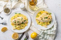 two white plates topped with chicken and pasta next to lemons, garlic and pepper