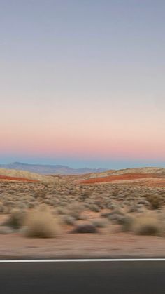 an empty road in the middle of nowhere with mountains in the distance and blue sky