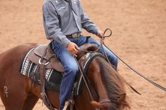 a young man riding on the back of a brown horse in an open dirt field