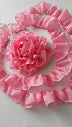 a large pink flower on top of a white cloth covered table with beaded trim