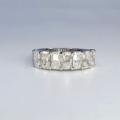 a white gold ring with five princess cut diamonds set in the center, on a plain surface