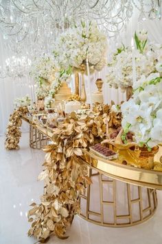 a table topped with lots of white flowers and gold leafy decorations on top of it