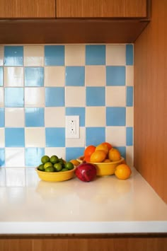 bowls of fruit are sitting on the counter in front of a blue and white tile backsplash