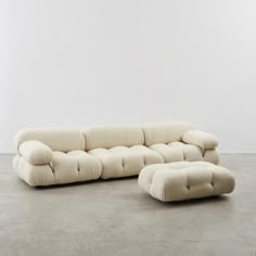 a white couch and ottoman sitting on top of a cement floor next to a wall