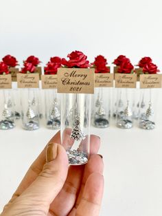 a hand holding a wine glass with red roses in it and merry christmas tags on the top