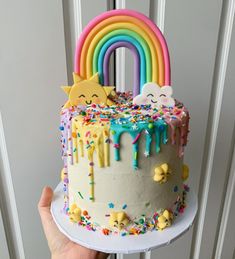 a hand holding a cake with sprinkles and rainbow decorations