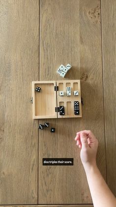 a wooden box filled with dice and dominos on top of a wood floor next to a person's hand