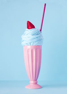 a pink cup filled with whipped cream and a strawberry on top, sitting on a blue surface