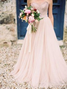 a woman standing in front of a blue door wearing a dress and holding a bouquet