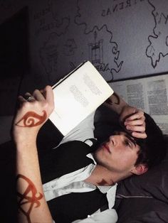 a man laying down reading a book with tattoos on his arm