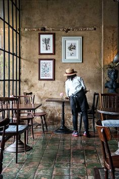 a woman standing in front of a table with chairs and pictures hanging on the wall