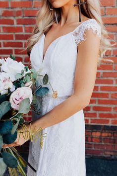 a woman holding a bouquet of flowers in front of a brick wall