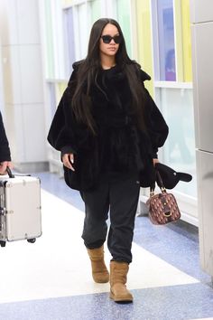 a woman with long black hair and sunglasses carrying a suitcase in an airport terminal area