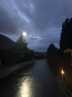 an empty street at night with lights on the side and dark clouds in the background