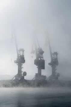 several large cranes are in the foggy water