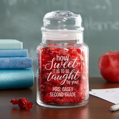 a glass jar filled with red candy next to books and an apple on a desk